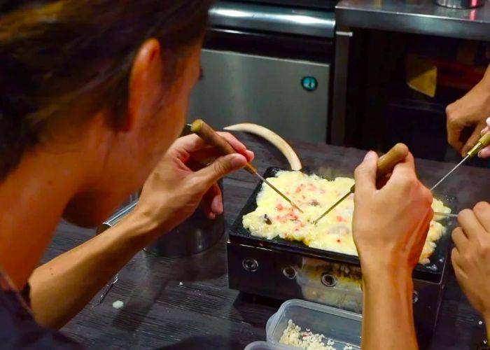 A guest on a takoyaki cooking class, using two tools to move batter around.